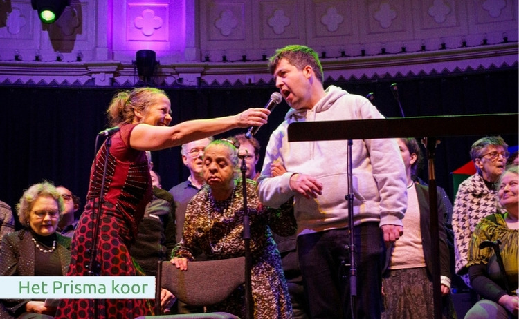 Meerdere leden van het Prisma koor aan het zingen op het podium.